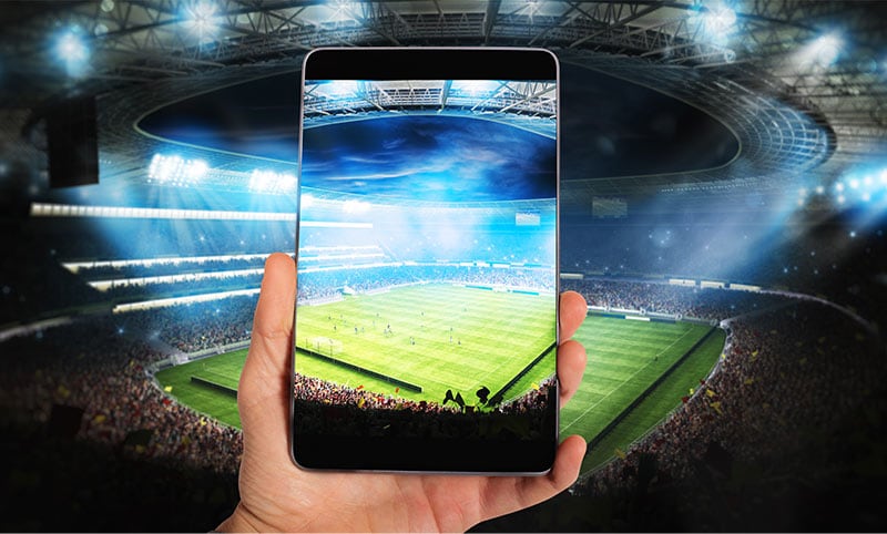 A hand holding a tablet up inside of a stadium recording it