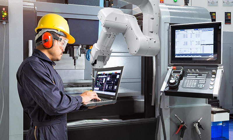a man in a yellow hard hat looking at a readout next to a automation robot