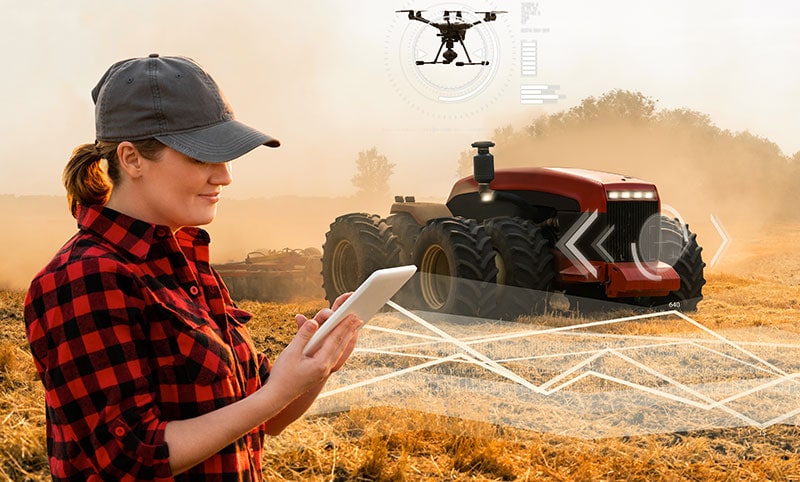 lady farmer looking at a tablet with an automated tractor and drone in the background