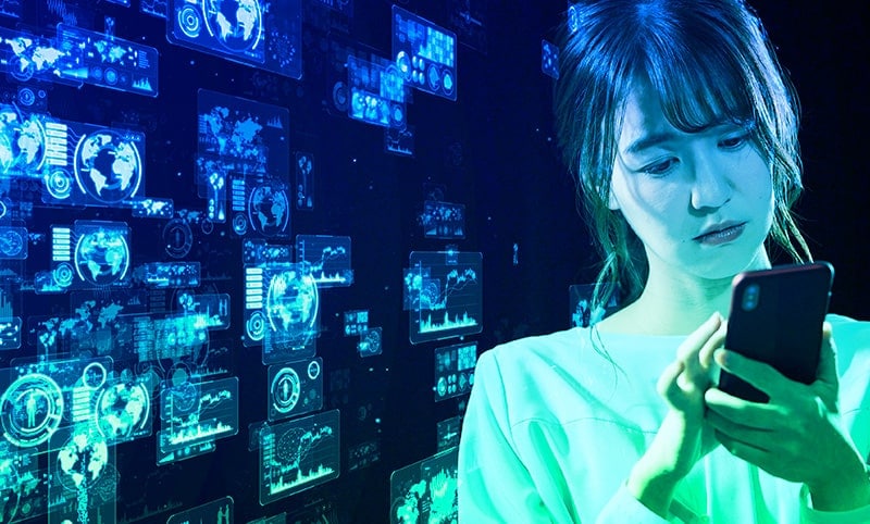 a woman in the foreground looking and interacting with her phone and in the background are virtual screens showing various world maps