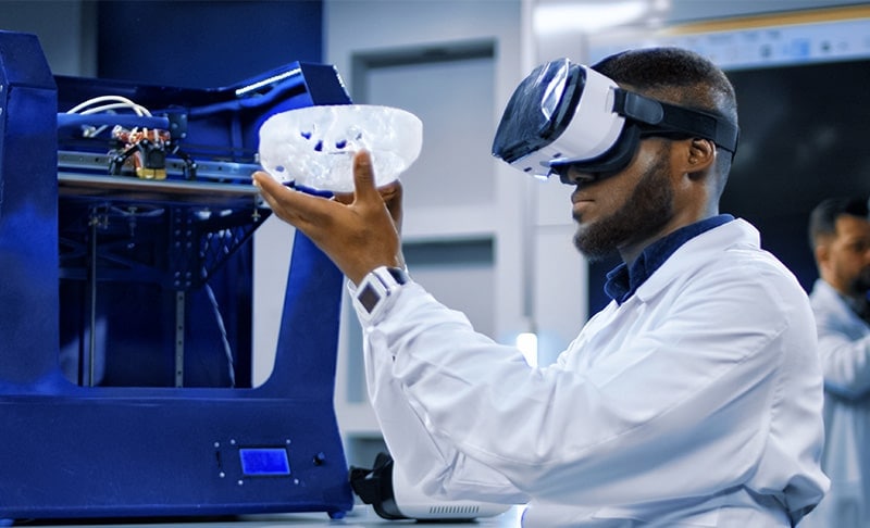 An engineer wearing VR goggles and holding a 3D-printed model in the air inspecting it