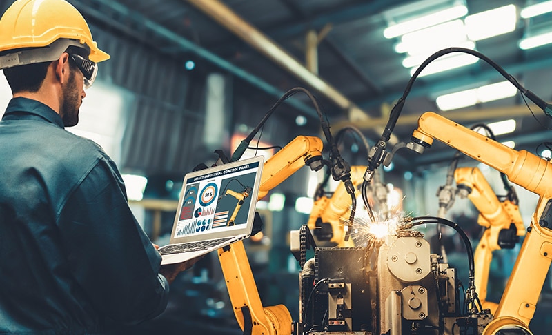 Man controling robot arms as they weld in factory setting