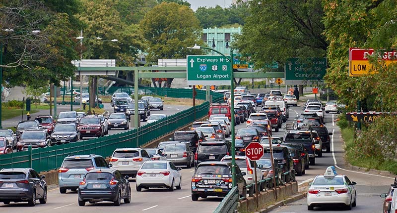 View of a busy highway full of cars. The road passes by rows of lush trees.