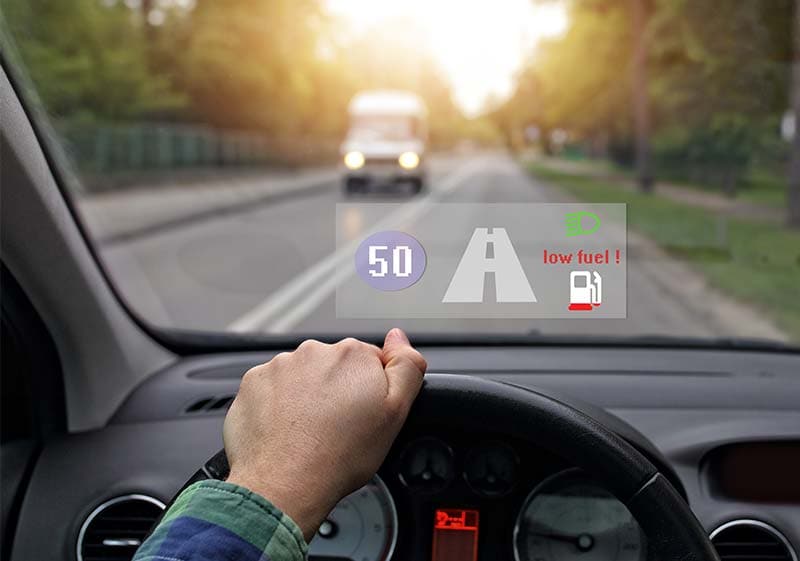 the inside of a car showing a hand on the wheel and the speed of 50, low fuel and a projection of the road on the window